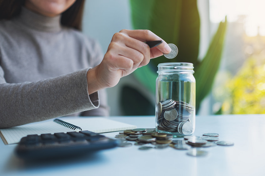 Closeup image of a woman putting coins in a glass jar with calcu